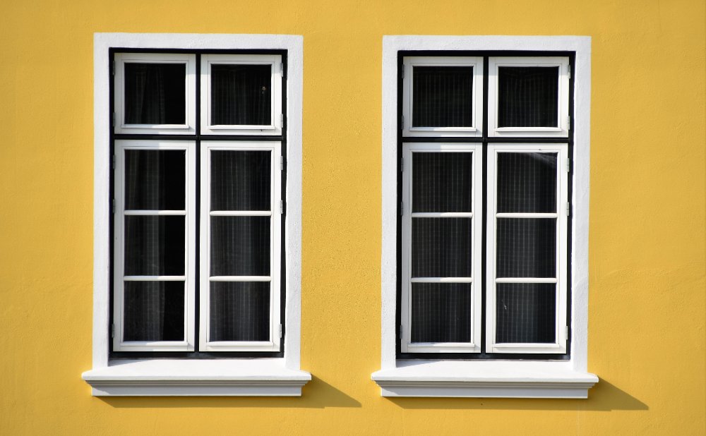 Zwei Fenster nebeneinander, gelbe Hauswand
